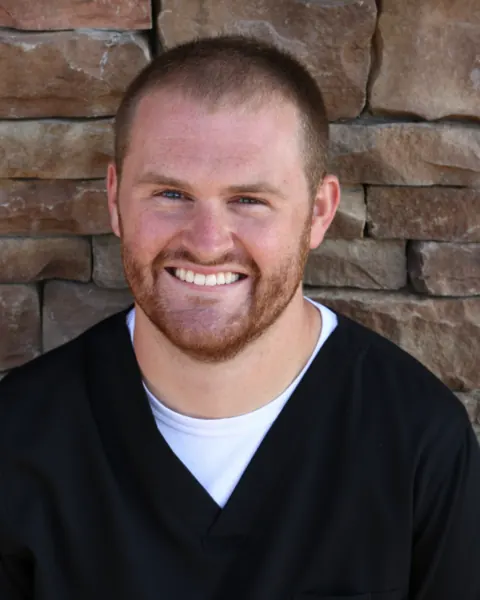 Dr. Jameson Klavins, DDS, smiling in black scrubs in front of a stone wall